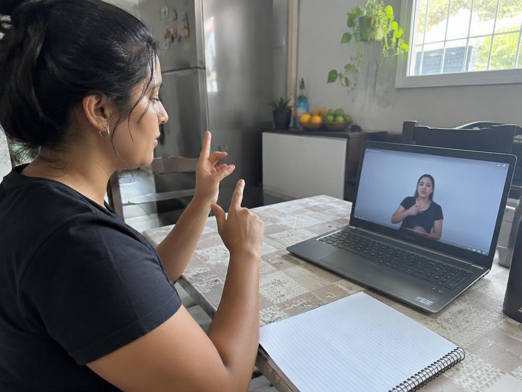 Mulher praticando sinais de Libras sozinha em casa, em frente ao notebook
